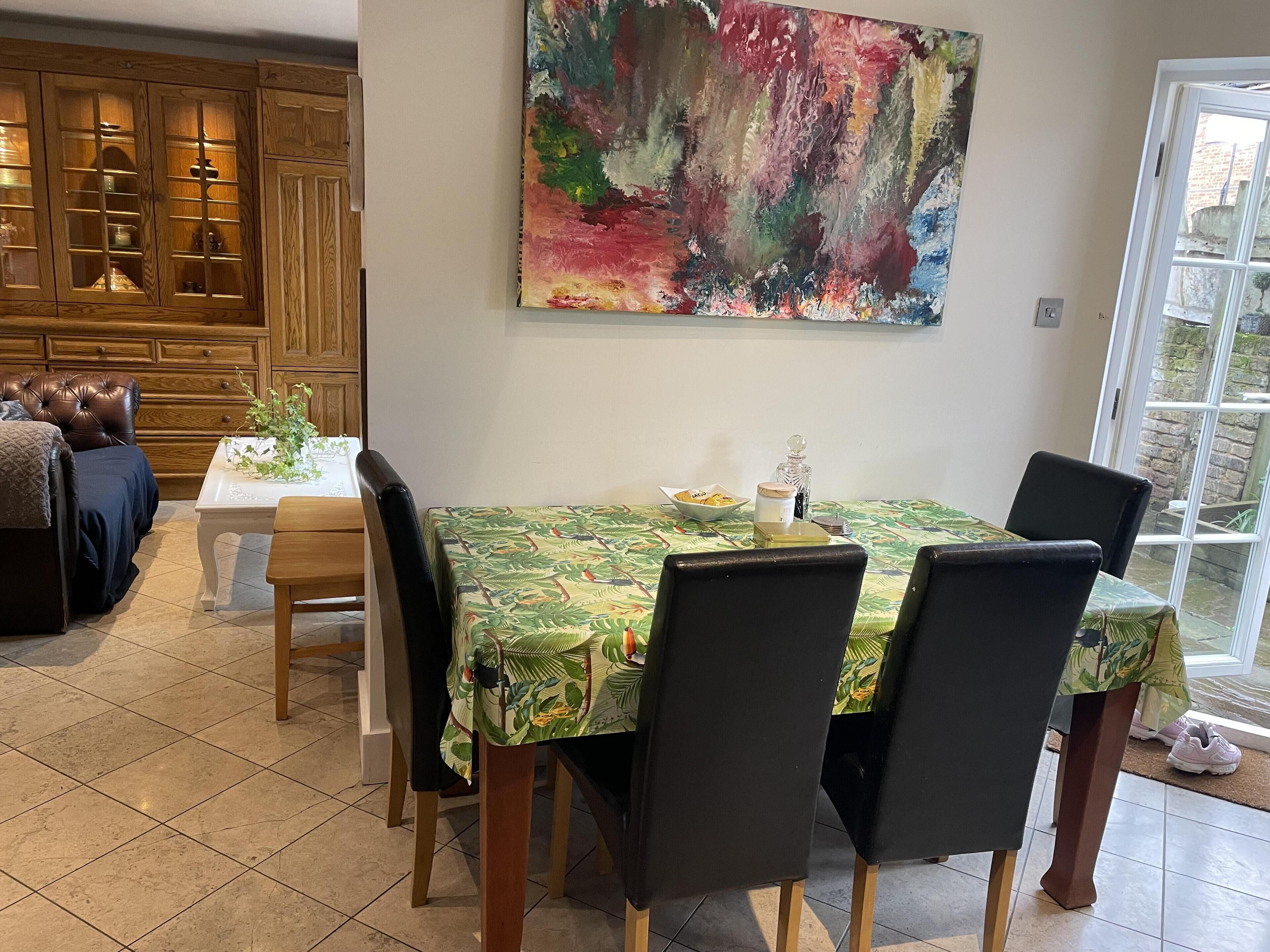A dining area with a table set for four, surrounded by chairs. A large abstract painting hangs above the table.