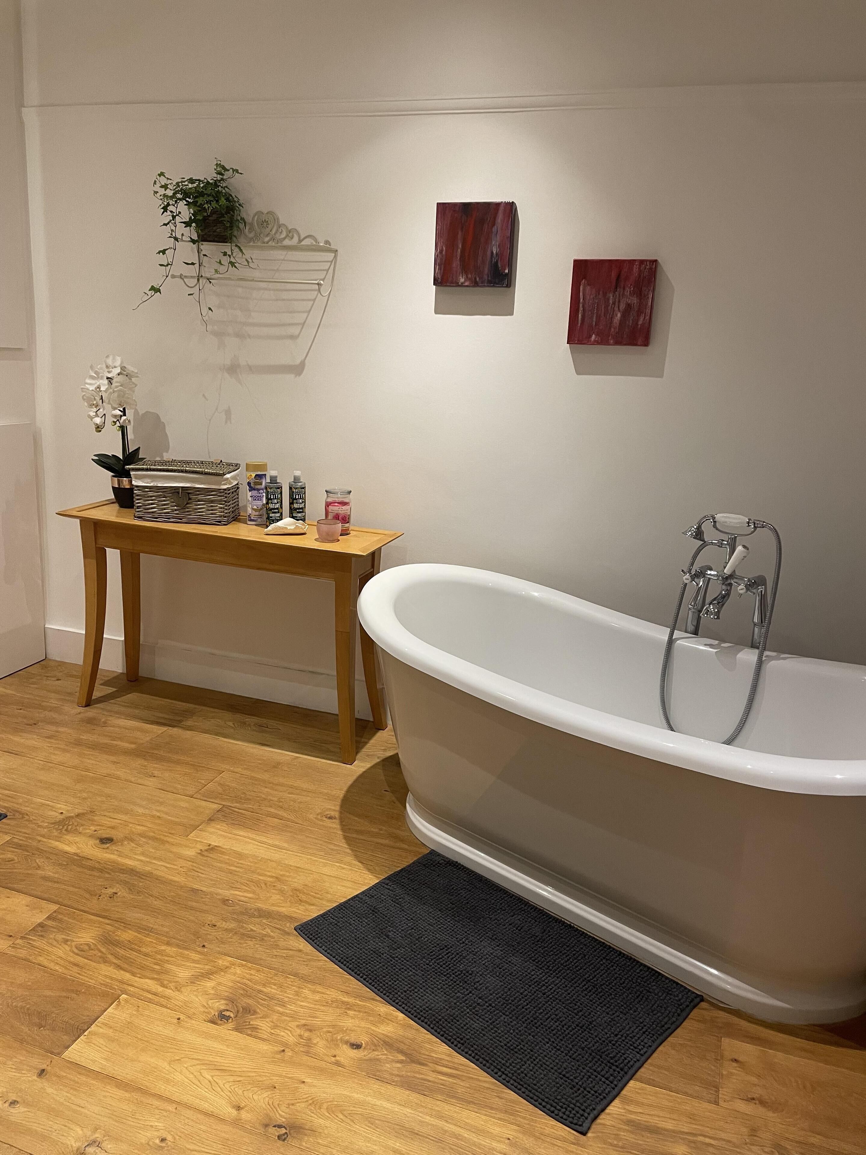 A bathroom with a freestanding bathtub, a wooden table with toiletries, and a small potted plant.