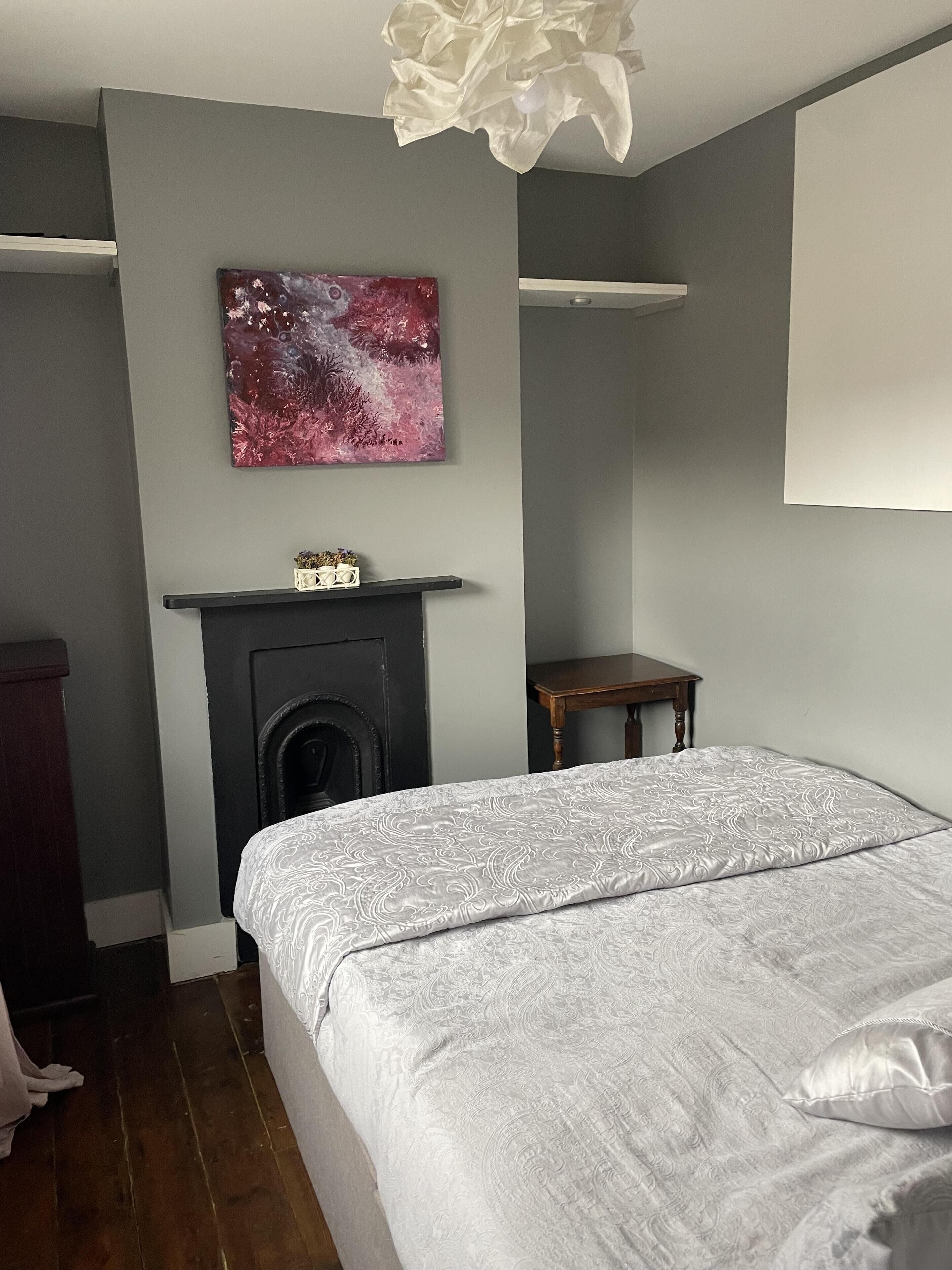 Une chambre à coucher avec un lit, une cheminée, une petite table et une étagère fixée au mur.