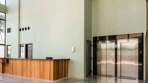 A reception area with a wooden reception desk, a large window, and a pair of elevators. - ILUSION VISTA PANORÂMICA (Natal)