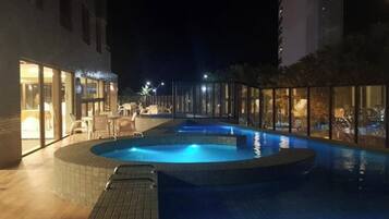 Piscina interna com borda revestida em azulejo, rodeada por paredes de vidro e um deck de madeira.