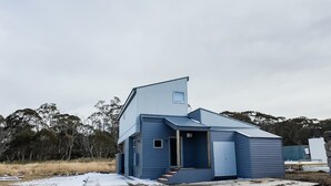 A modern blue house with a unique triangular roof, a small porch, and a visible door. - Fimian - Dinner Plain (Dinner Plain)