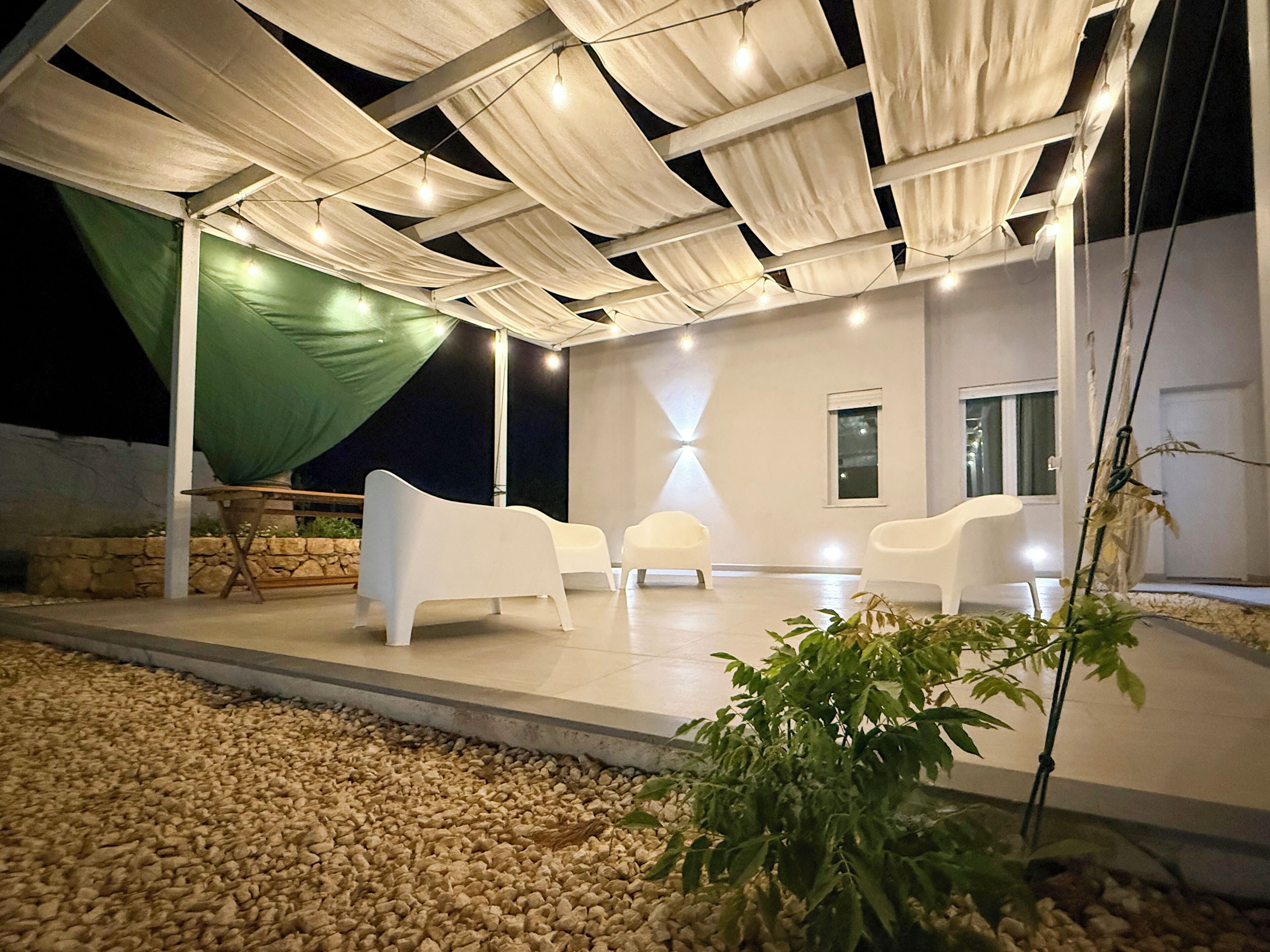 Un espace extérieur aménagé en terrasse, avec des chaises blanches, une table et un auvent vert.
