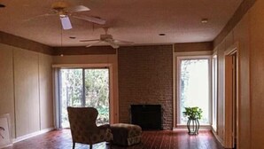 A spacious room with hardwood flooring, a fireplace, a ceiling fan, and large windows. - 2-bedroom apartment in enchanting Fort Worth with AC (Fort Worth)