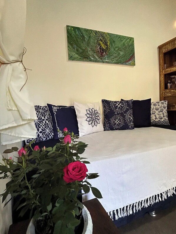 A neatly arranged bedroom with a bed, decorative pillows, a wall art piece, and a potted plant with flowers. - Pousada Villa dos Tucanos Camburi (Praia de Camburí São Sebastião)