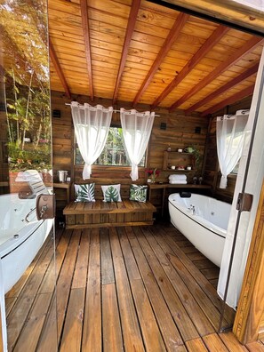 A wooden cabin with a wooden deck, two hot tubs, a bench with cushions, and a window with sheer curtains. - Pousada Villa dos Tucanos Camburi (Praia de Camburí São Sebastião)