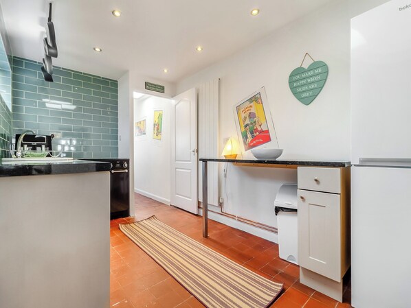 A modern kitchen with a black countertop, white cabinets, and a tiled backsplash. There is a sink with a faucet, a dish rack, and a stove. A rug is on the floor, and a heart-shaped decoration hangs on the wall.