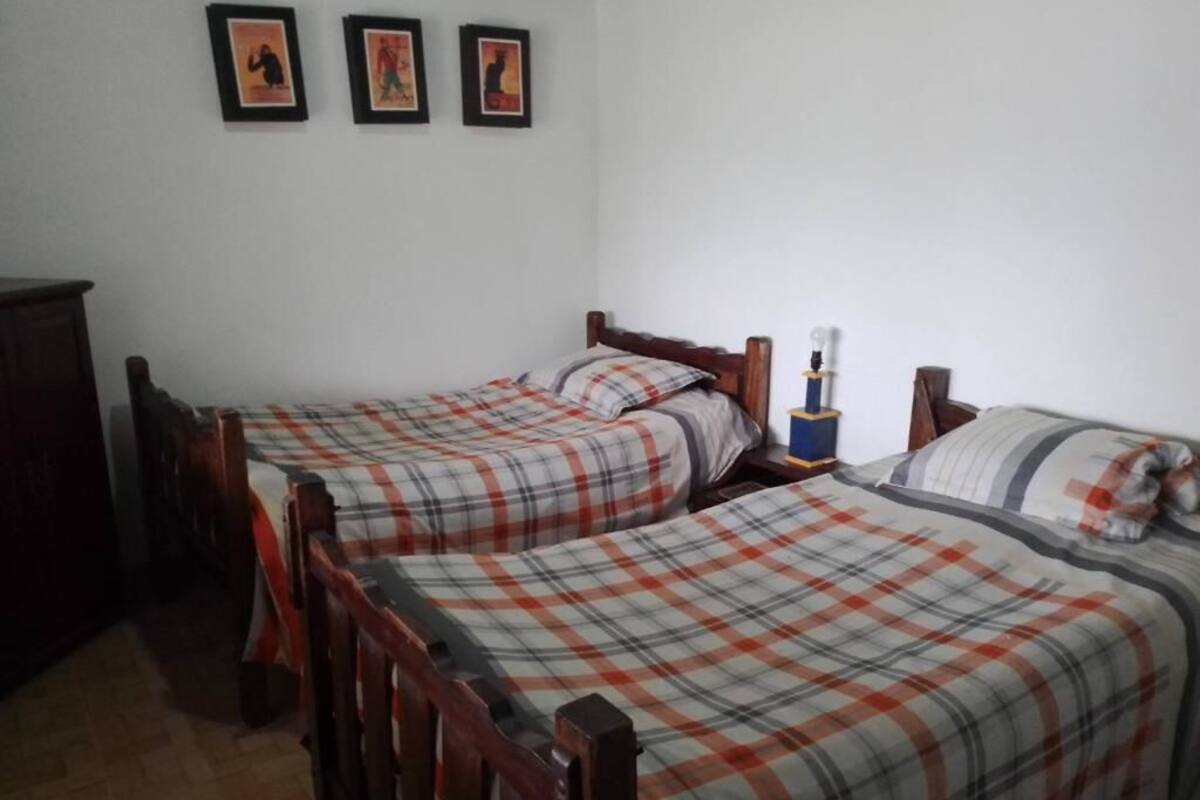 A room with two wooden beds, each with a plaid bedspread, a nightstand with a lamp, and a dresser.
