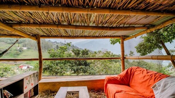 A room with a bamboo roof, a cushioned seating area, and a view of a green landscape. - Finca Umnisa  Choachi (Choachí)