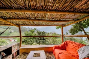 A room with a bamboo roof, a cushioned seating area, and a view of a green landscape. - Finca Umnisa  Choachi (Choachí)