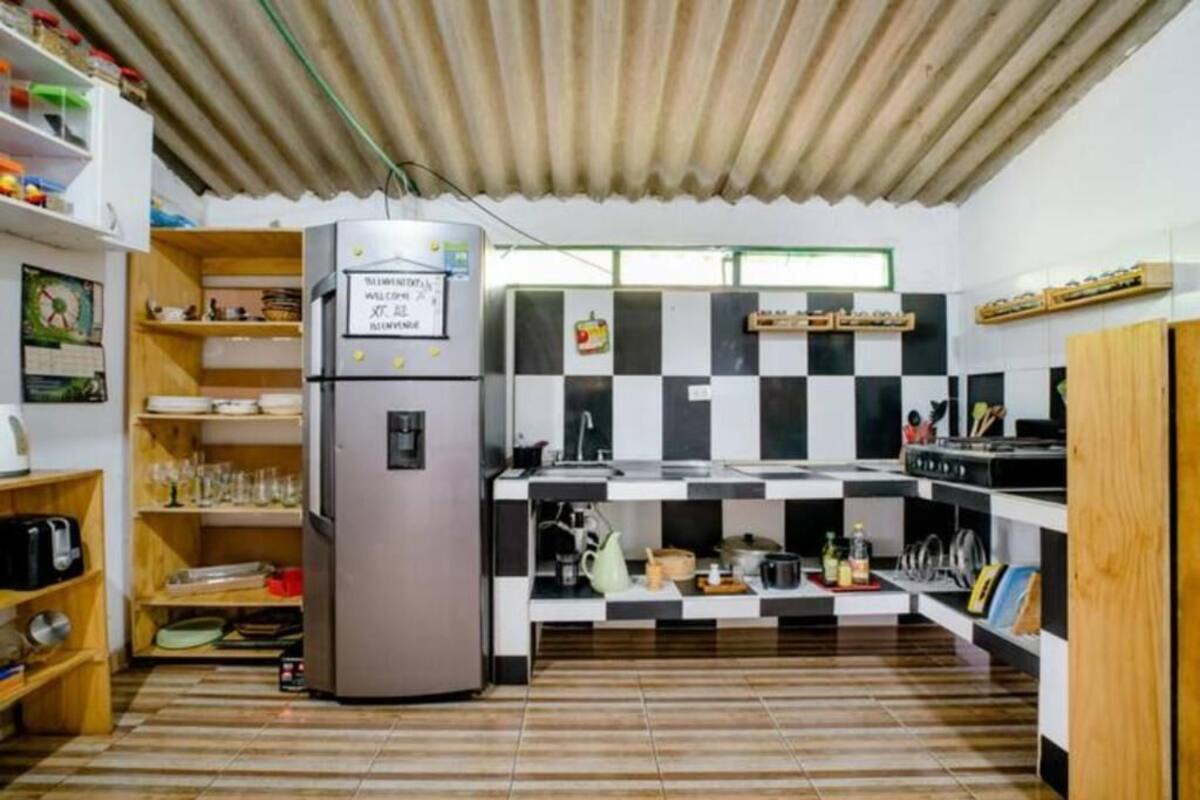 A compact kitchen with a refrigerator, checkered backsplash, and wooden shelves.