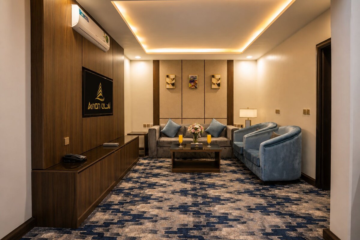 Un hall d’hôtel comprenant un comptoir d’accueil, un ensemble de canapés, deux fauteuils, une table basse agrémentée de fleurs et une moquette à motifs.