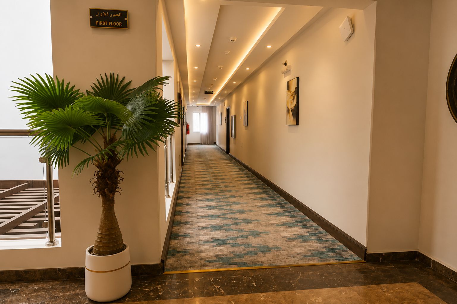 A hotel corridor with a palm tree, a 'First Floor' sign, and a patterned carpet.