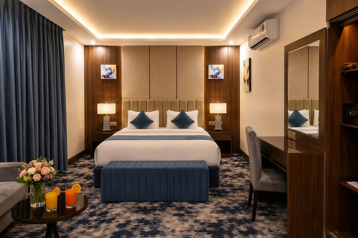 Une chambre d’hôtel avec un grand lit, deux tables de chevet avec des lampes, un bureau, une chaise, un miroir et un vase décoratif avec des fleurs.