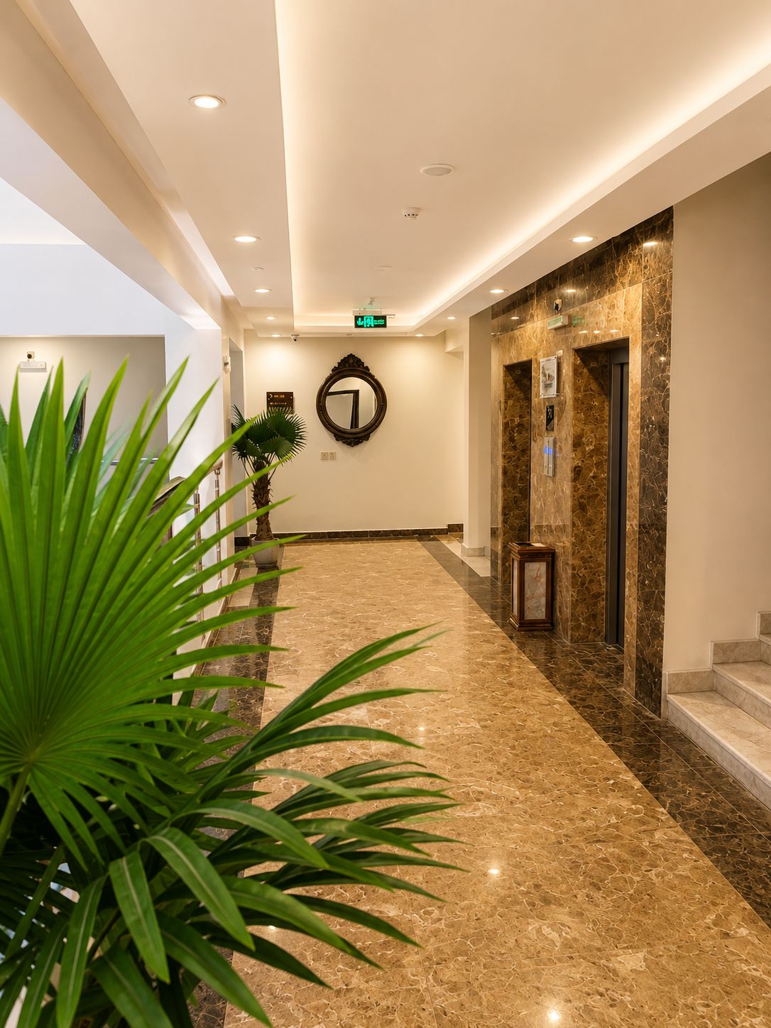 A hotel lobby with a marble floor, a reception desk, a wall-mounted mirror, and an elevator.
