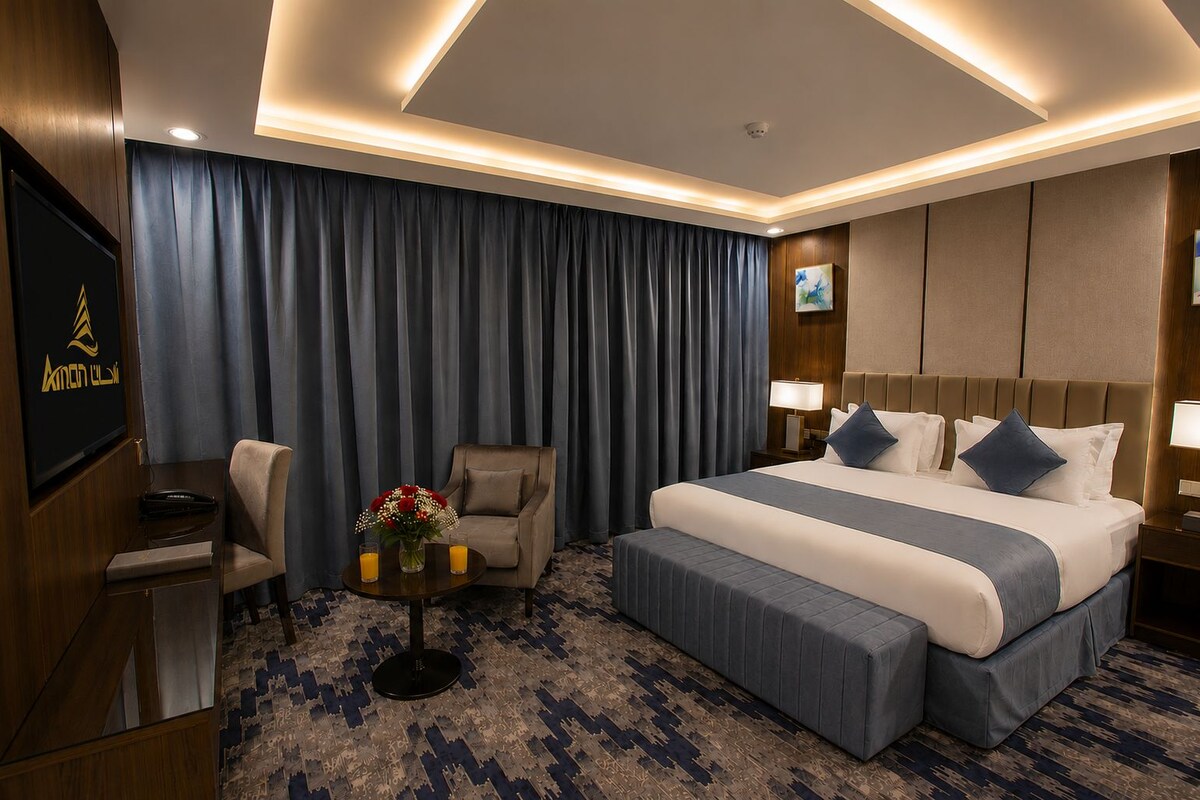 Une chambre d’hôtel avec un lit, une chaise, un bureau, une télévision et une petite table sur laquelle est posé un vase de fleurs.
