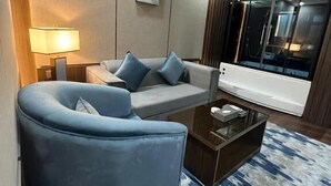 A modern living room with a blue sofa, a coffee table, and a large window with a view of a ship. - Aman Hotel Almhalh (Abha)