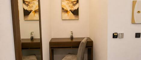 Habitación de hotel con escritorio, silla, banco, dos cuadros, un espejo y una lámpara de techo.
