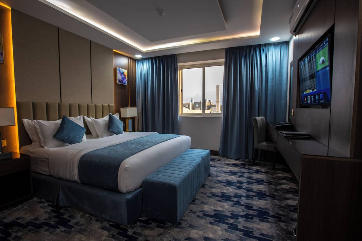 A modern hotel room with a large bed, a desk, a TV, and a view of the cityscape.