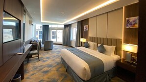 A hotel room with a large bed, a desk, a chair, a TV, and a window. - Aman Hotel Almhalh (Abha)