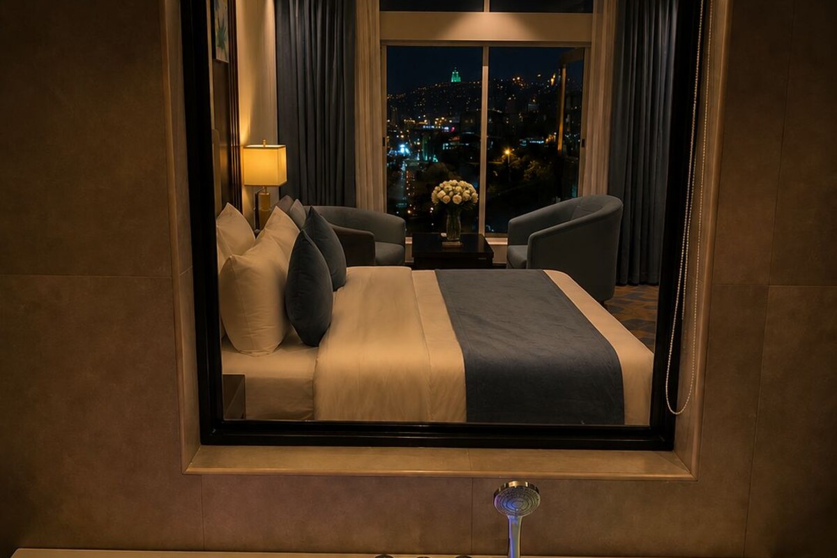 Une chambre d’hôtel dotée d’une grande fenêtre, d’un lit, d’un coin salon et d’une baignoire avec des lumières colorées.