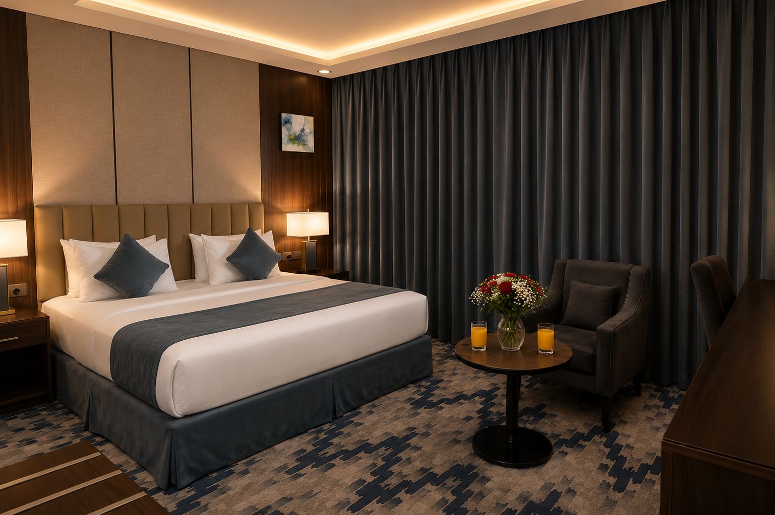 Ein Hotelzimmer mit einem großen Bett, einem Schreibtisch, einem Stuhl und einem kleinen Tisch mit Blumen.