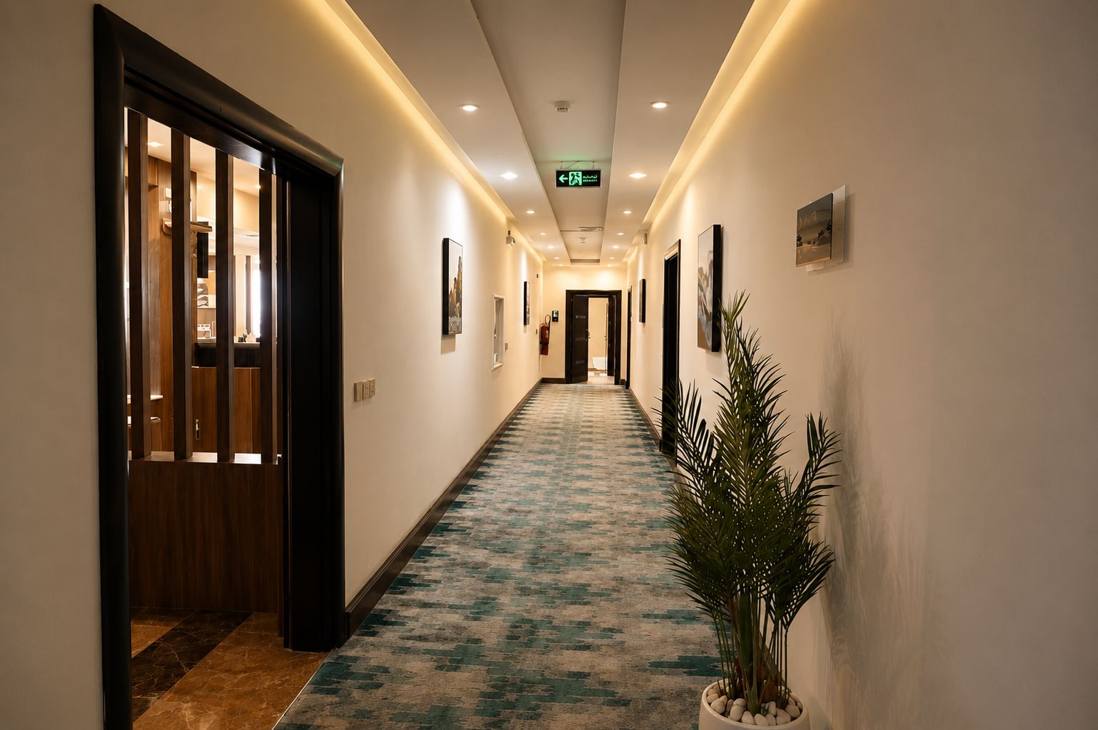 Ein Hotelkorridor mit einem gemusterten Teppich, Holztüren und gerahmten Bildern an den Wänden.