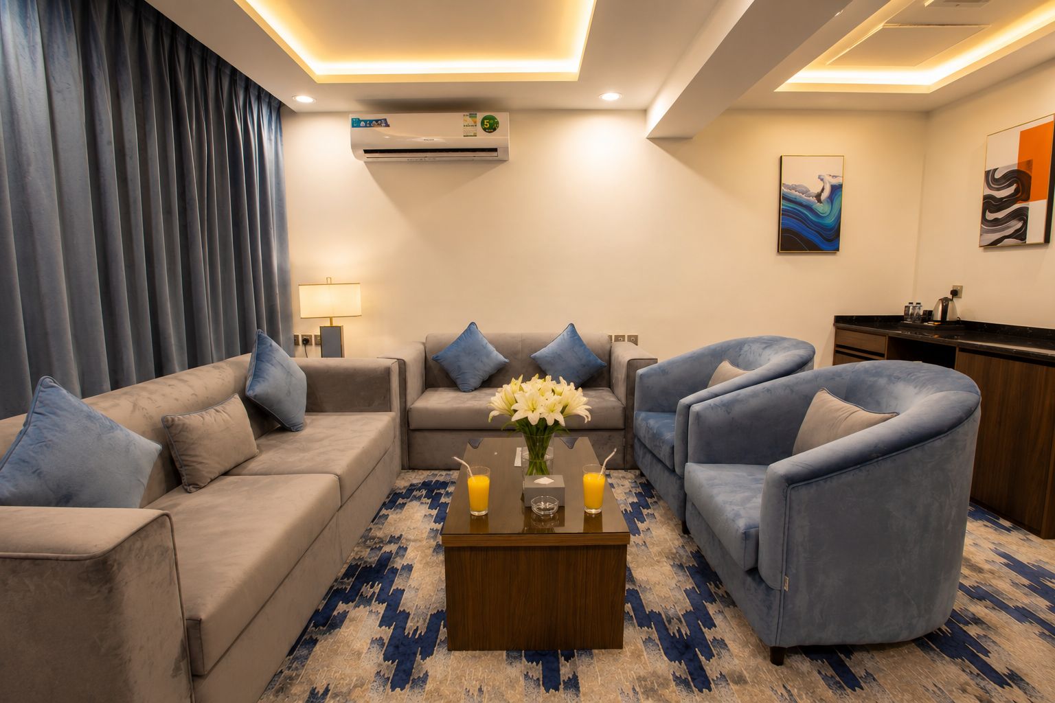 Una sala de estar moderna con un sofá, sillones, una mesa de centro con flores y un aire acondicionado instalado en la pared.