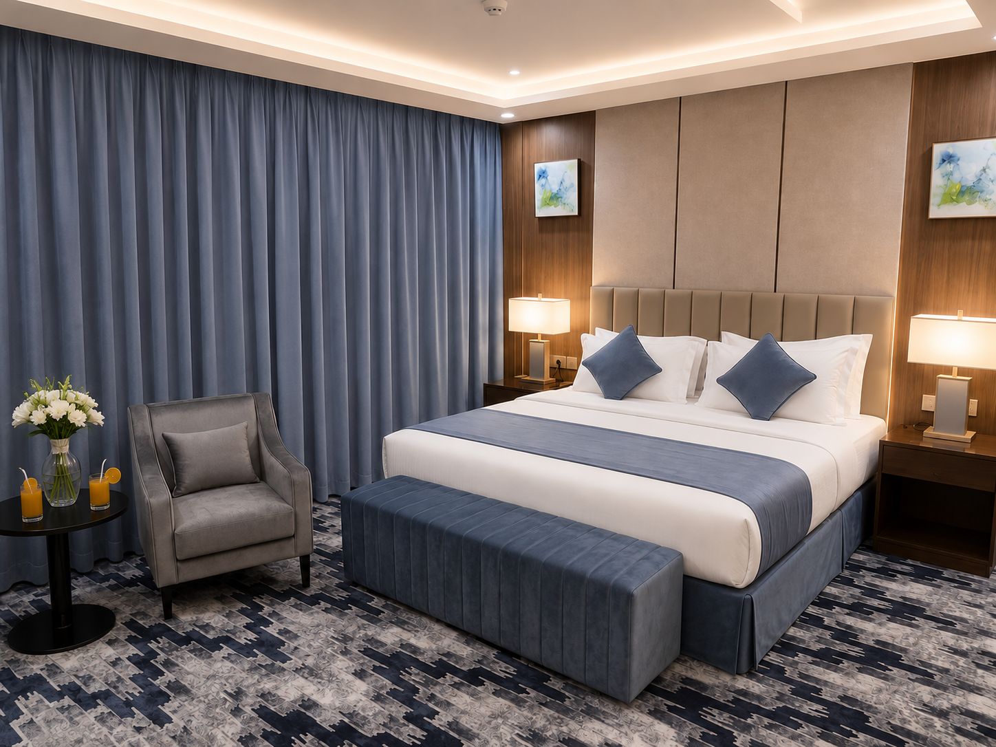 A hotel room with a large bed, a chair, a small table with drinks, and artwork on the walls.