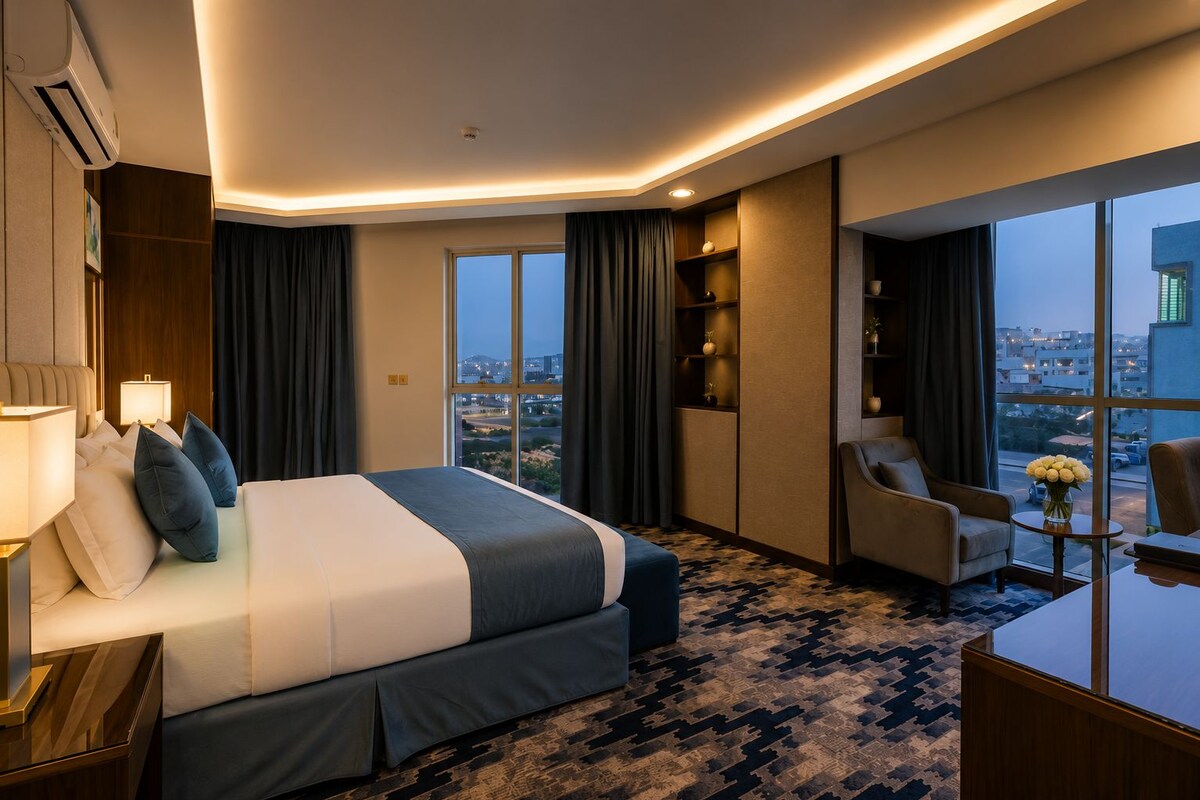Une chambre d’hôtel avec un grand lit, un bureau et une chaise. Il y a une fenêtre donnant sur la ville.