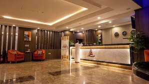A hotel lobby with a reception desk, two red armchairs, a large potted plant, and a marble floor. - Aman Hotel Almhalh (Abha)