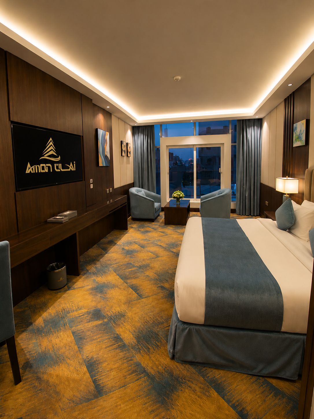 Een hotelkamer met een groot bed, een bureau met stoel, een televisie en uitzicht op de stad 's nachts.