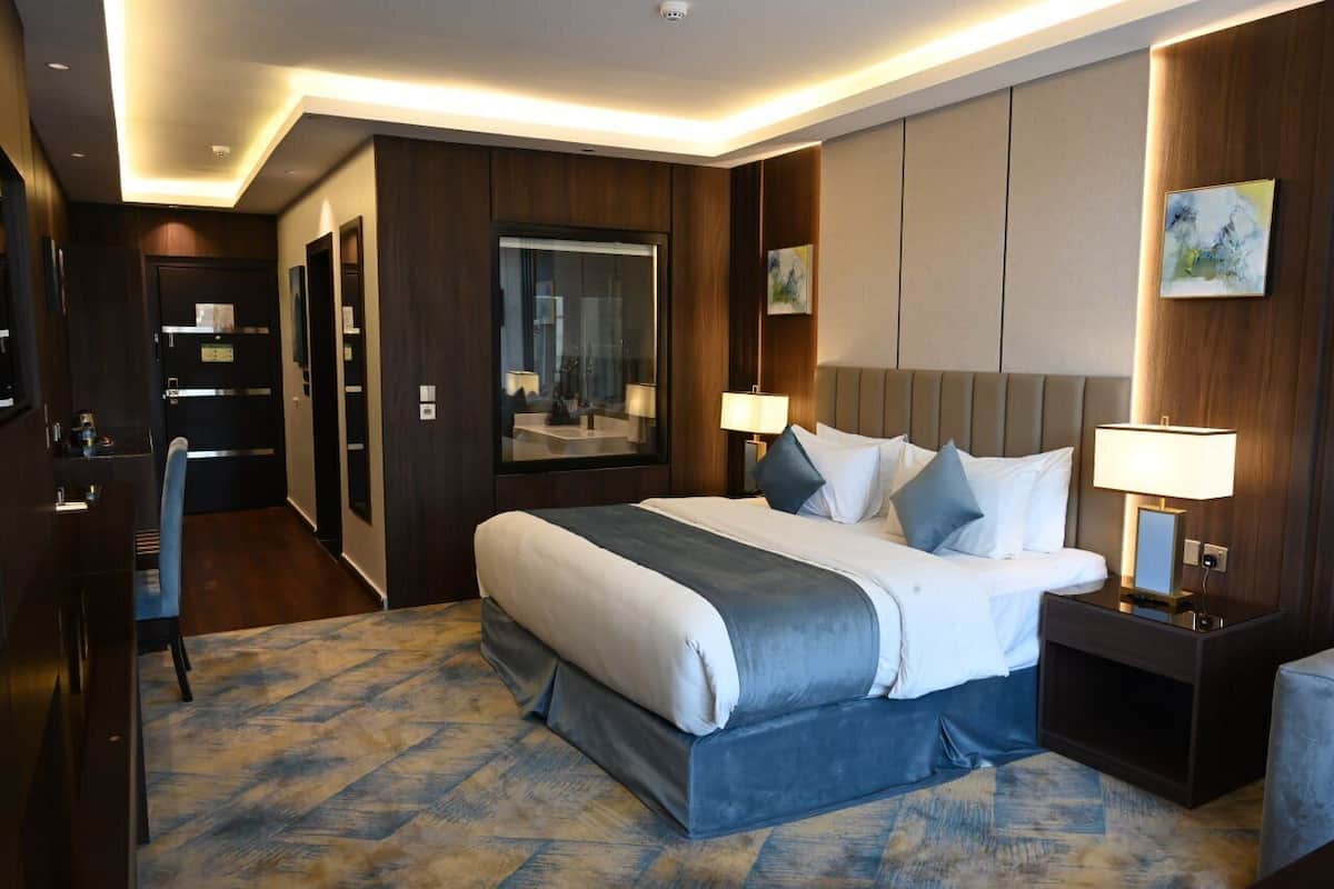 A hotel room with a large bed, bedside lamps, a desk, and a chair.