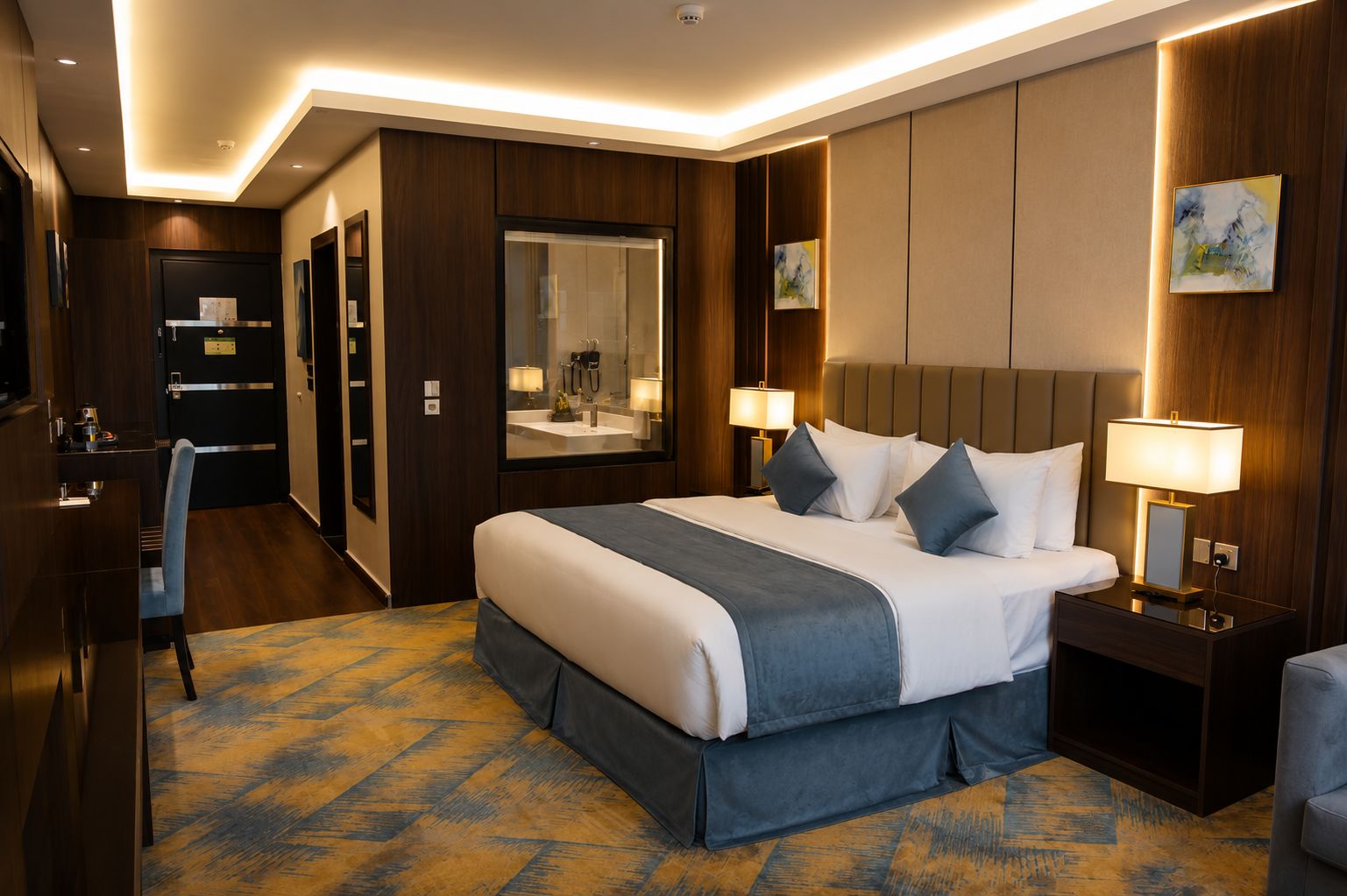 Una habitación de hotel con una cama grande, lámparas de noche, un escritorio y un espejo.