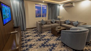 A modern hotel room with a sofa, armchairs, a TV, and a large window with curtains. - Aman Hotel Almhalh (Abha)