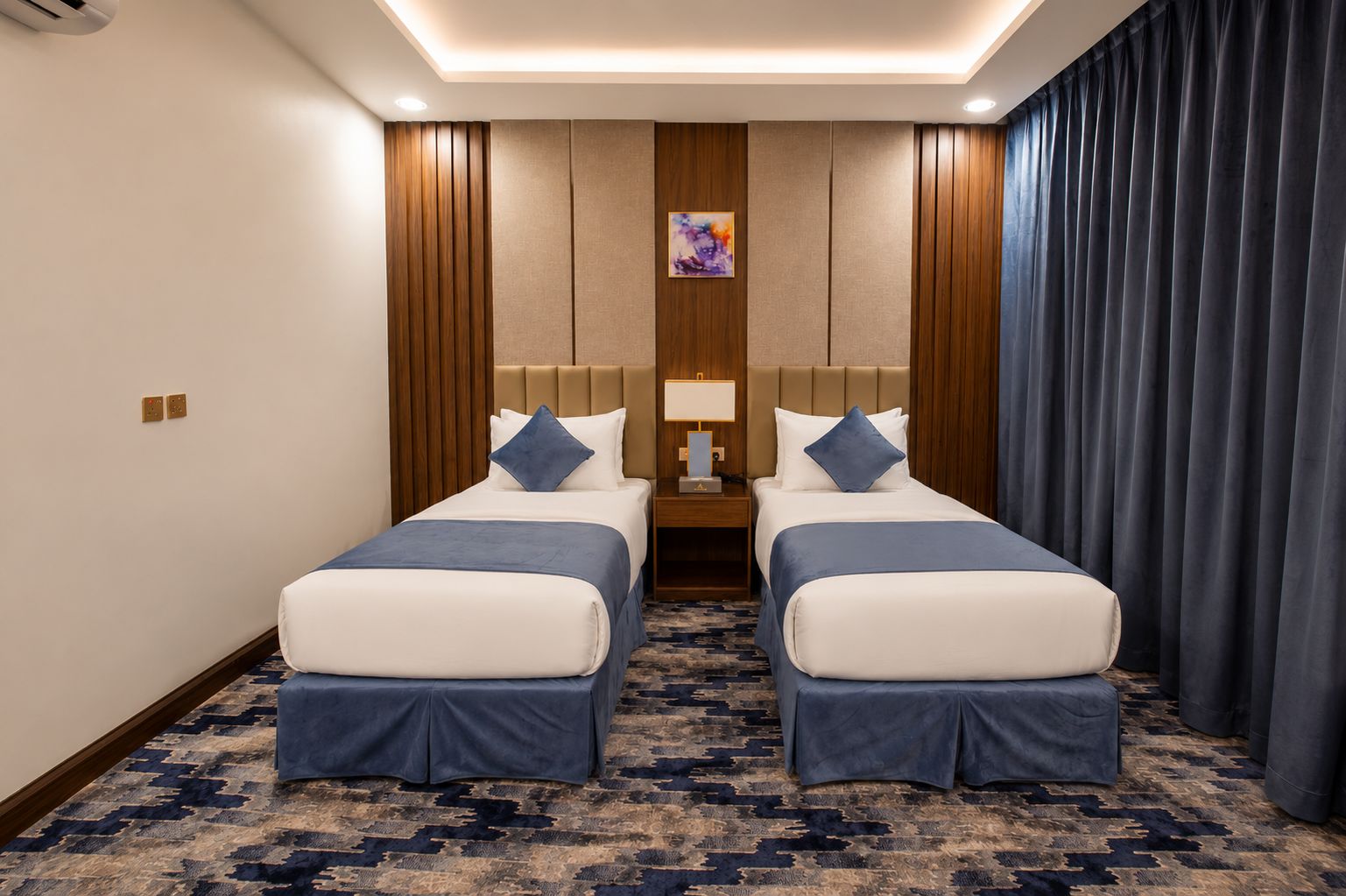 A hotel room with two beds, a nightstand, a lamp, and a painting on the wall.