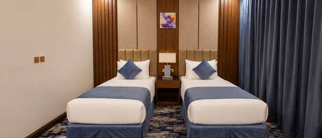A hotel room with two beds, a nightstand, a lamp, and a painting on the wall.