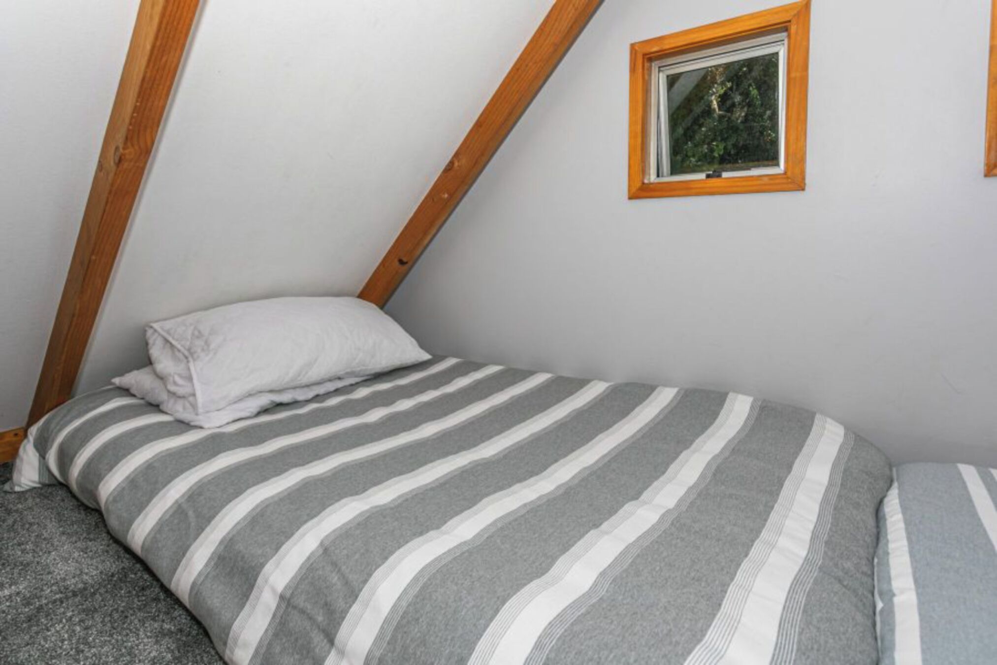 A small, single-bed room with a sloped ceiling and a window with a wooden frame.