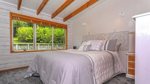 A bedroom with a large window, a bed with a patterned headboard, and a nightstand.