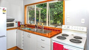 A compact kitchen with white cabinets, a wooden countertop, a sink, a stove, and a window with a view of greenery.