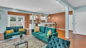 Un salon spacieux avec des canapés de couleur turquoise, une table basse en verre et un coin cuisine à l’arrière-plan.