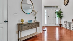 Un couloir avec une console en bois, un globe terrestre et un miroir. Une porte se trouve à côté, et un pot de fleurs est posé près de celle-ci.