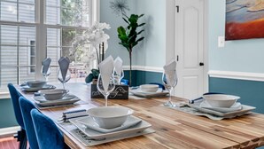 Une table à manger dressée avec de l’assiette blanche, des bols et des verres, entourée de chaises bleues.
