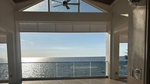 A spacious balcony with a view of the sea, a ceiling fan, and a sign indicating maximum occupancy. - New! Just renovated coastal condo, Gated community, 10 min to beach by shuttle!  (Bonita Springs)