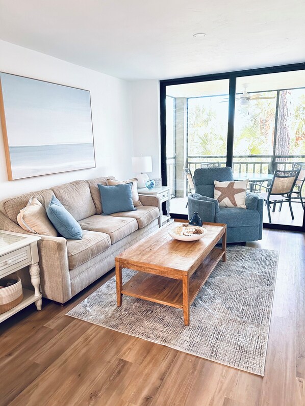 Ein geräumiges Wohnzimmer mit einer Couch, einem Couchtisch und Blick ins Freie durch große Fenster.