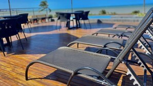 Zona junto a la piscina con sillones reclinables y sombrillas, con vista a una masa de agua.