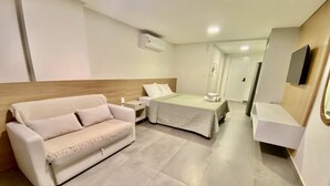 Una habitación de hotel moderna con una cama, un sofá, una mesita de noche y un televisor montado en la pared.