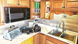 Eine Küche mit Holzausstattung, einer Mikrowelle, einem Toaster, einem Mixer und einem Spülbecken.