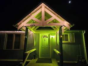 Una casa con puerta verde, el número 4974 sobre la puerta, y un porche con un banco.