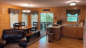 Une cuisine chaleureuse, aménagée dans le style d’un chalet, avec des meubles en bois, un coin repas doté d’un fauteuil en cuir et une grande fenêtre agrémentée de rideaux.